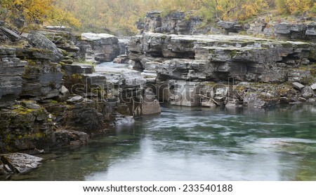Short river and rapids up North. Canyon with rocks and cliffs surrounded by colorful trees, moss in autumn, fall colors.