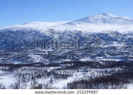 View of a village opposite the valley. Clean white snow, mountain birch forest and covered landscape. Treeline, timber line on the slope.