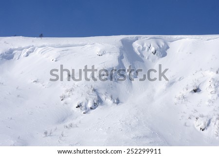 Sunny day on a slope in the Scandinavian mountains. Clean white snow and steep covered cliffs, rocks.