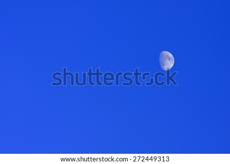 Blue moon of the Nordic bright sky. Half moon against a bright blue afternoon sky.