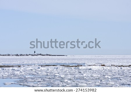 Coast, coastline and shore of the Baltic Sea in March during the day, hours when the ice at sea breaks up. Sunny day by the sea. Lighthouse, beacon in the background.