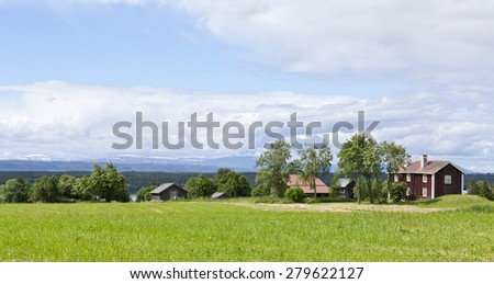 Great-Lake area Sweden in sunny June and July. Buildings at a farm, agriculture place. Farmland, fields this side in sunshine. Lake and mountains in the background. Falu red paint main building.