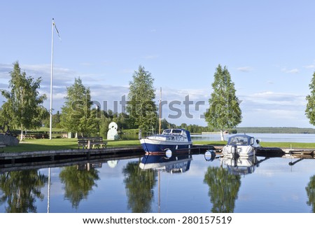 GREAT-LAKE, SWEDEN ON JULY 02. View in a sunny evening at a small harbor on July 02, 2012 by the Great-Lake, Sweden. Calm water and the boats are moored by the bridge. Park to the left.