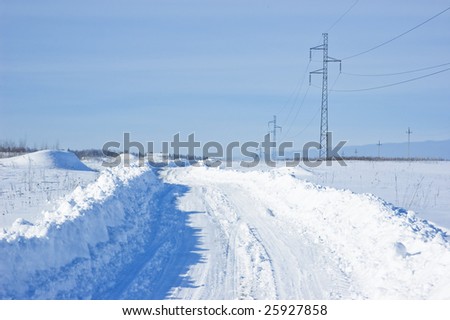 Snow-covered winter road with power line in the field, Russia