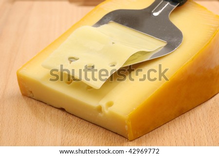 cheese slicer slicing through a block of cheese on a wooden cutting board