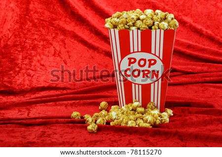 caramel popcorn in a decorative red and white popcorn cup on a red velvet background