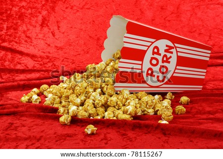caramel popcorn in a decorative red and white popcorn cup on a red velvet background