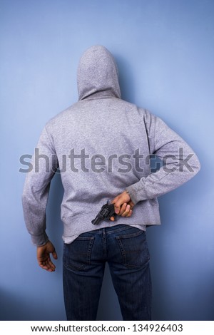 Hooded man hiding gun behind his back