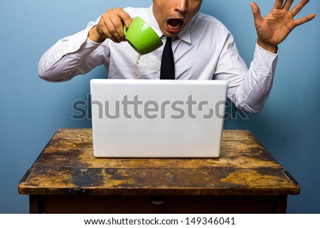 Clumsy businessman spilling coffee on his laptop computer