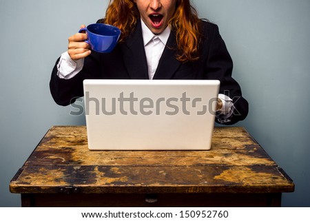 Shocked businesswoman nearly spilling coffee on her laptop