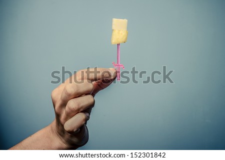 Hand holding cocktail stick with cheese and pineapple
