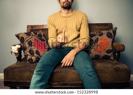 Young man on sofa displaying obscene gesture