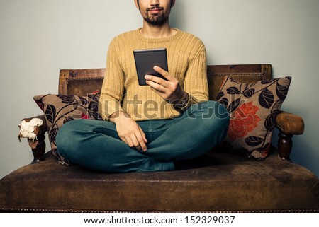Young man sitting on sofa reading on tablet