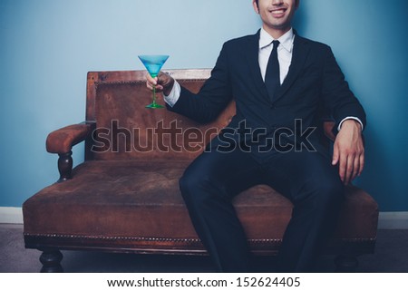 Happy businessman on sofa drinking cocktail
