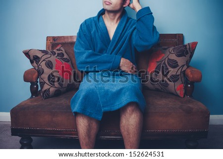 Young man in robe on sofa scratching his head