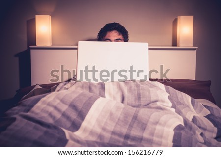 Man is sitting in bed behind his laptop Man is sitting in bed behind his laptop