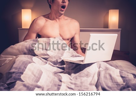 Young man is sitting in bed and watching pornography on laptop