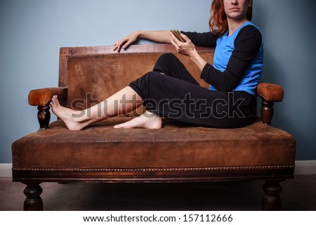Young woman sitting on old antique sofa holding her phone