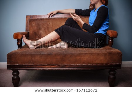 Young woman sitting on old sofa texting on her phone