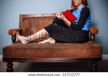 Young woman sitting on old sofa reading a book