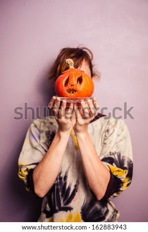 Young woman with scary pumpkin in front of her face