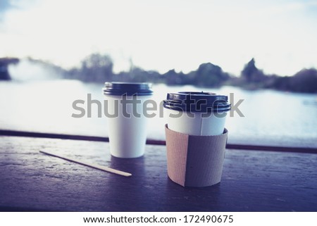 Two paper coffee cups by a lake