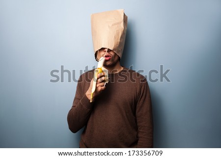 Young man with bag over head eating banana
