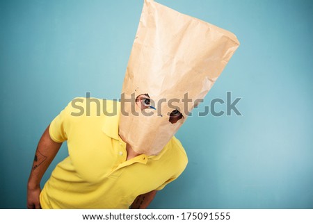 Young man with a paper bag over his head is looking at the camera through his eye holes