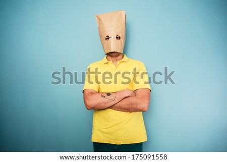 Young man with a bag over his head standing with his arms crossed