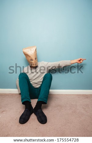 Man with a bag over his head is sitting on the floor and pointing