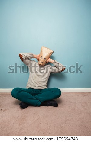 Man with a bag over his head is sitting on the floor and covering his ears