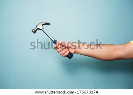 A young man\'s hand is holding a hammer against a blue wall