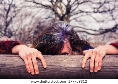 A young woman is hiding behind a wooden beam in the park