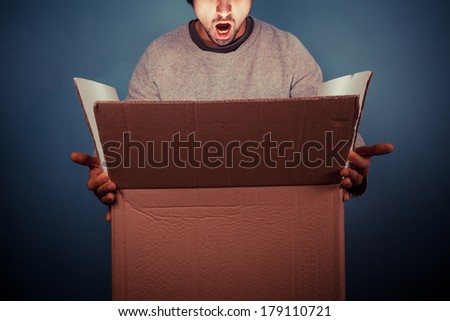 Surprised young man is opening a large cardboard box with something exciting inside it