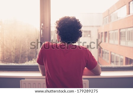 Young man is at the windowsill and looking out at sunset