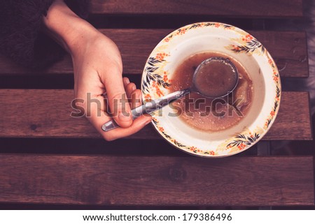 A woman is holding a spoon and eating soup, closeup on her hand