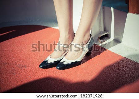 Closeup on a young woman\'s feet and shoes as she is standing on the red deck of a ship