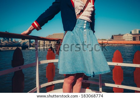 A young woman\'s skirt is blowing in the wind as she is standing on the deck of a boat cruising down the river