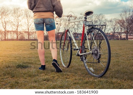 A young woman is walking on the grass in the park with her bicycle