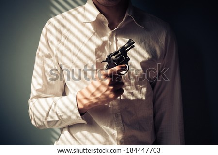 Young man with gun by the window is covered in shadows from the blinds