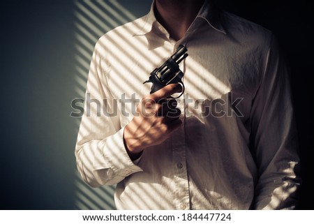 Young man with gun by the window is covered in shadows from the blinds