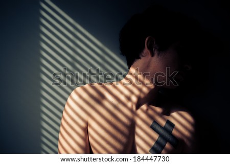 Sad naked man sitting by the window with shadows from blinds on his face