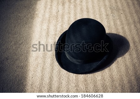 A bowler hat on the floor with shadows from the venetian blinds across it