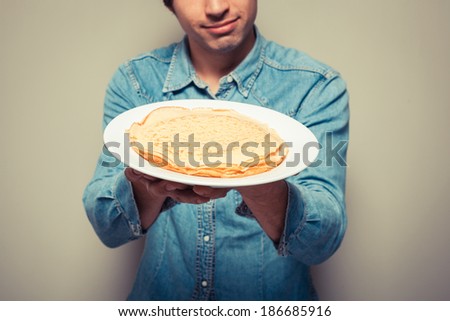 Young man is presenting a plate with a stack of pancakes