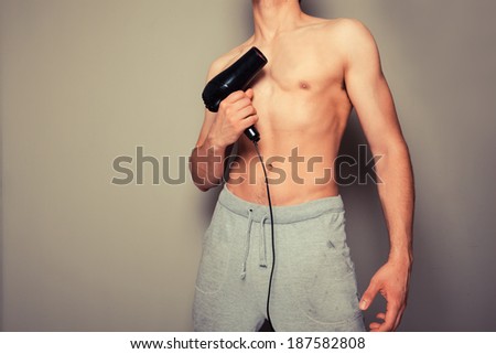 Athletic young man is holding a hair dryer and messing around with it