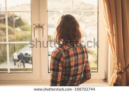 Young woman is standing and looking out the window