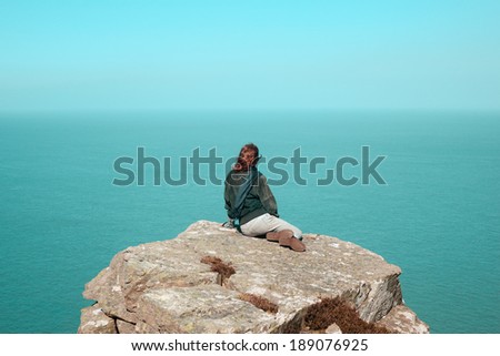 Young woman is sitting on a cliff by the sea