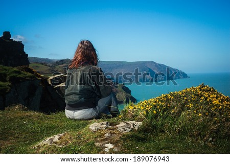 Young woman is sitting on the edge of a cliff by the sea
