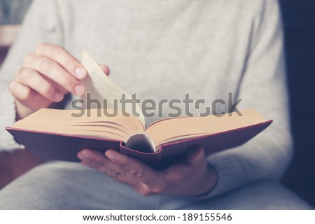 Young man is sitting on a sofa and flipping the pages of a big book