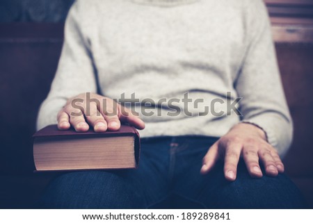 Young man is sitting on a sofa with his hand on a big book